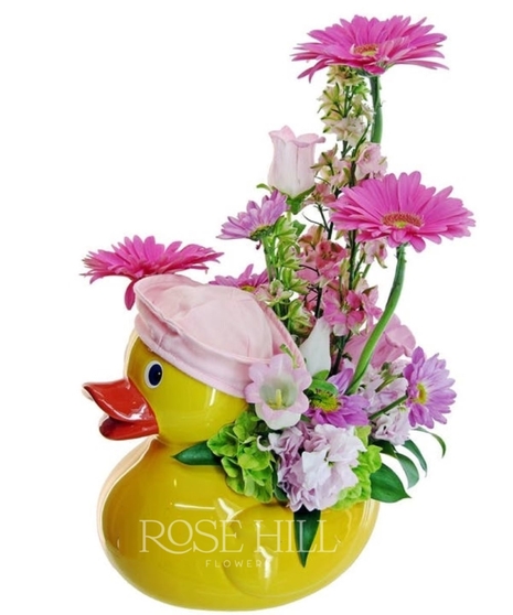 Yellow duck container with pink or blue fresh florals for new baby.