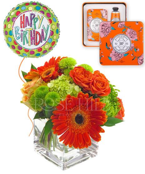 A mix of yellow, orange and green blossoms in a clear glass cube vase